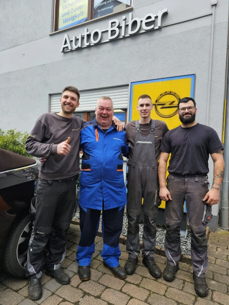 Vier Mitarbeitende von Auto Biber stehen vor dem Firmengebäude in Adelsheim unter dem Schriftzug des Autohauses. Das Bild zeigt das Werkstatt- und Serviceteam in einem freundlichen, kollegialen Moment.